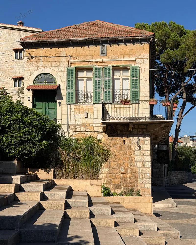 Lebanese stone house with a red-tiled roof, green shutters and an arched doorway