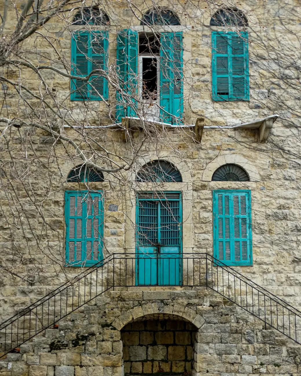 Traditional Lebanese sandstone house with arched windows and turquoise shutters