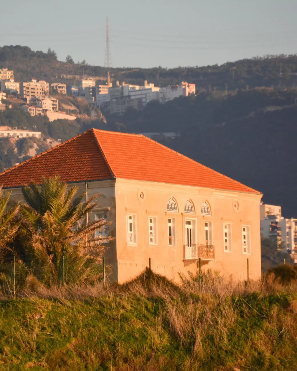 Red-roofed stone house on a hillside above the sea at sunset